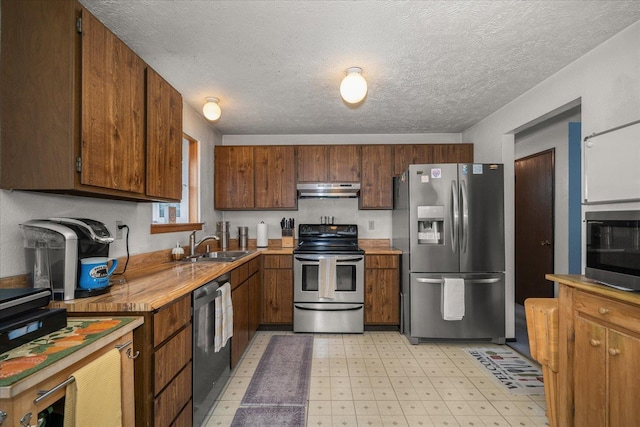 kitchen with light floors, a sink, under cabinet range hood, a textured ceiling, and appliances with stainless steel finishes