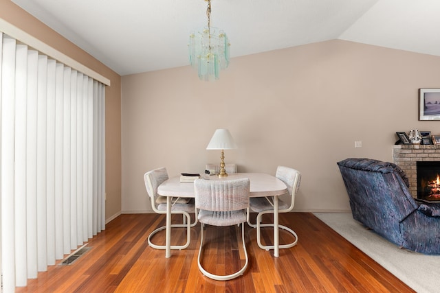 dining space with visible vents, wood finished floors, a fireplace, a chandelier, and vaulted ceiling