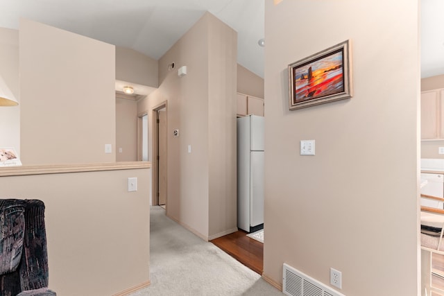 kitchen featuring baseboards, visible vents, freestanding refrigerator, vaulted ceiling, and carpet flooring