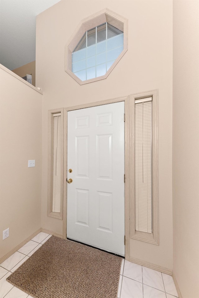 tiled foyer featuring baseboards and a towering ceiling