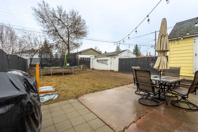 view of yard featuring an outbuilding, a patio, a trampoline, a fenced backyard, and outdoor dining area