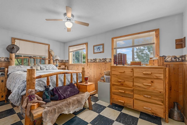 bedroom with tile patterned floors, a wainscoted wall, wooden walls, and ceiling fan