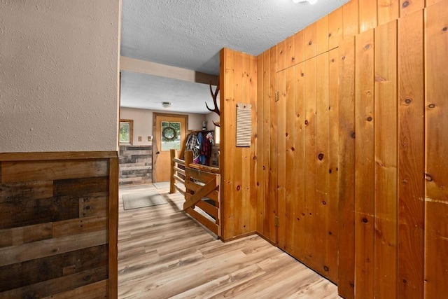 hallway with wood walls, a textured ceiling, light wood-type flooring, and a textured wall
