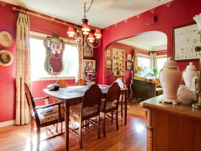 dining space featuring baseboards, arched walkways, a notable chandelier, and wood finished floors