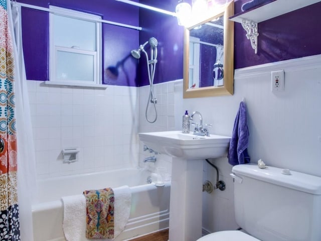 bathroom featuring a wainscoted wall, shower / bath combination with curtain, and toilet