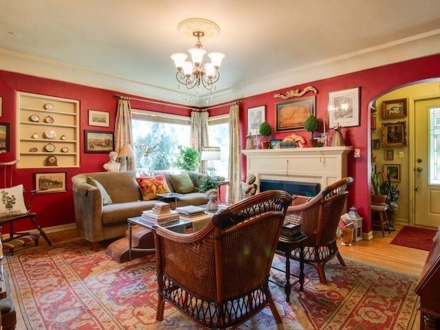 living room featuring built in features, wood finished floors, arched walkways, an inviting chandelier, and a fireplace