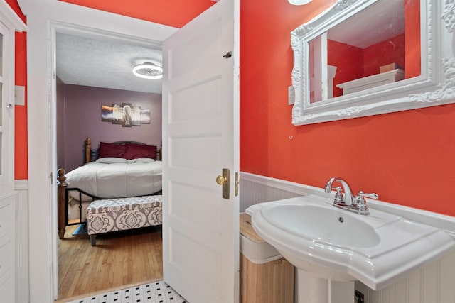 bathroom featuring ensuite bathroom, a sink, a textured ceiling, wood finished floors, and wainscoting