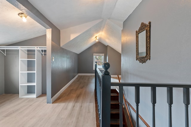 hall with an upstairs landing, vaulted ceiling, baseboards, and wood finished floors