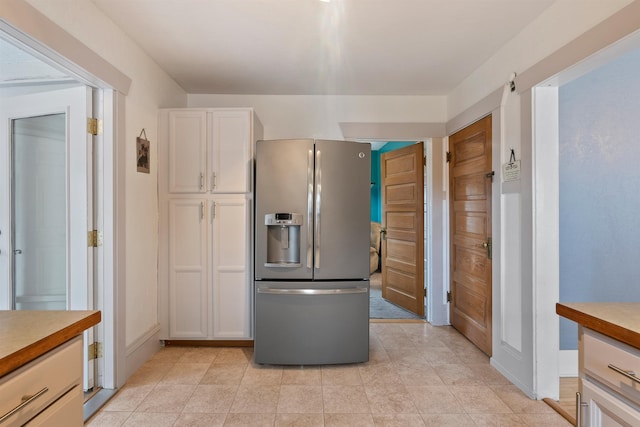 kitchen with stainless steel fridge, white cabinets, light countertops, and baseboards