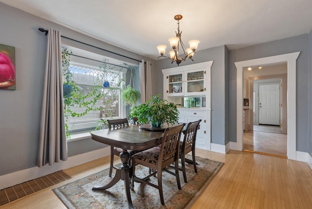 dining room featuring light wood-style floors, baseboards, a notable chandelier, and visible vents