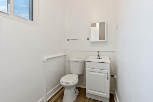 half bathroom featuring toilet, wood finished floors, tile walls, wainscoting, and vanity