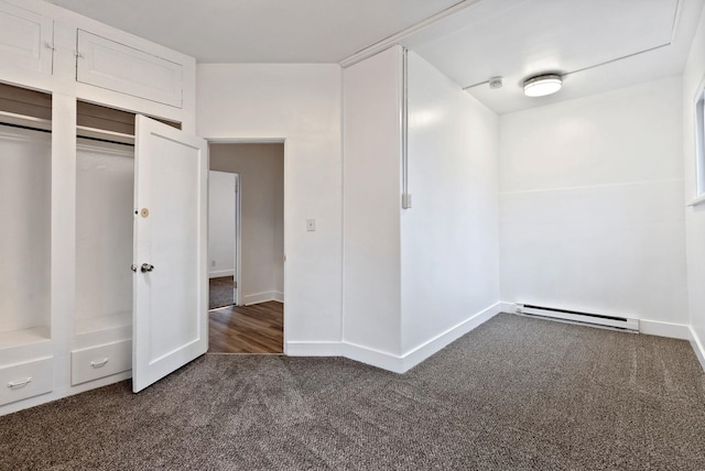 unfurnished bedroom with dark colored carpet, a baseboard heating unit, and baseboards