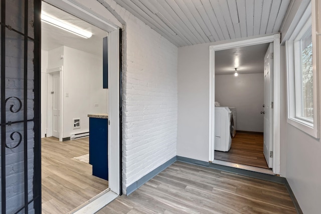 clothes washing area featuring brick wall, wood finished floors, laundry area, and washing machine and clothes dryer