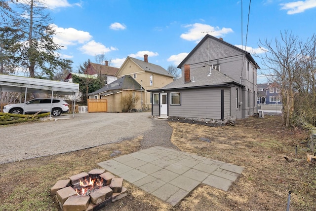 rear view of house featuring a carport, driveway, and an outdoor fire pit