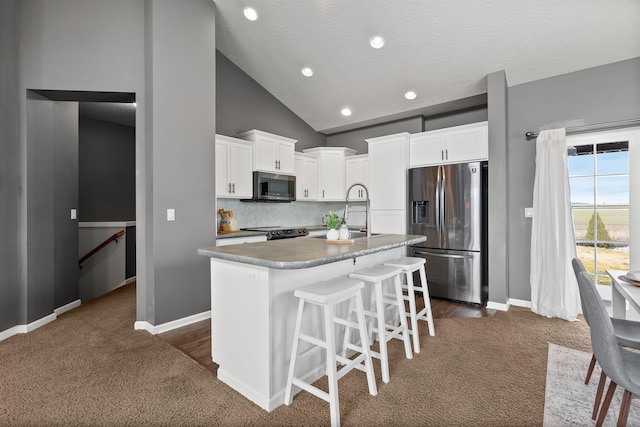 kitchen with a center island with sink, a sink, white cabinetry, appliances with stainless steel finishes, and decorative backsplash