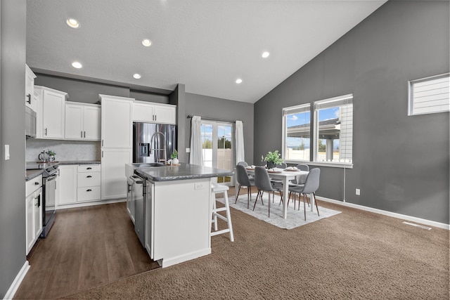 kitchen with stainless steel appliances, dark countertops, an island with sink, and white cabinetry