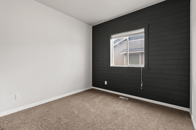 spare room with visible vents, baseboards, wooden walls, and carpet flooring