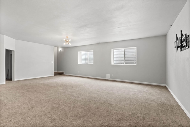 carpeted spare room featuring baseboards and a chandelier