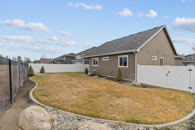 rear view of house with a yard, a fenced backyard, and a gate