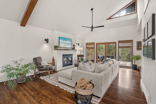 living area featuring dark wood finished floors, beamed ceiling, a glass covered fireplace, high vaulted ceiling, and a ceiling fan