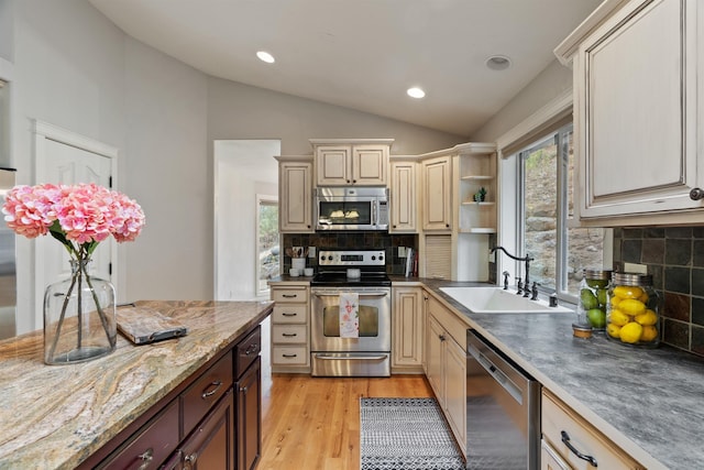 kitchen featuring light wood finished floors, vaulted ceiling, cream cabinets, stainless steel appliances, and a sink