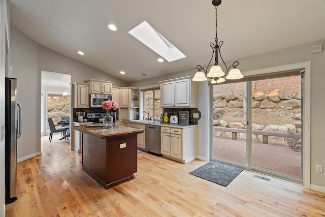 kitchen with lofted ceiling with skylight, a kitchen island with sink, light wood-style flooring, stainless steel appliances, and an inviting chandelier