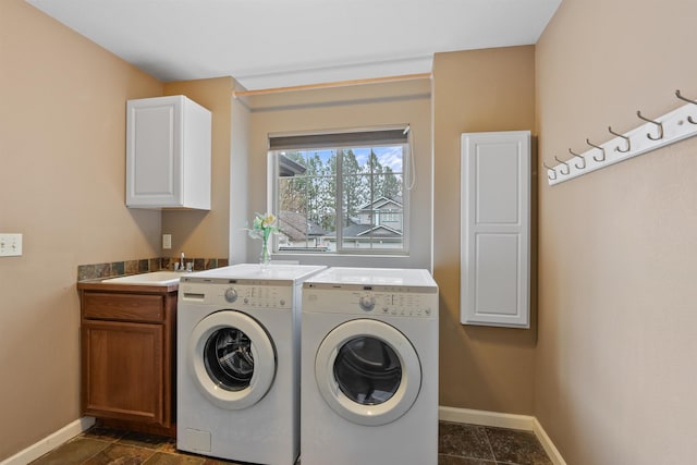 washroom with cabinet space, washing machine and dryer, baseboards, and a sink