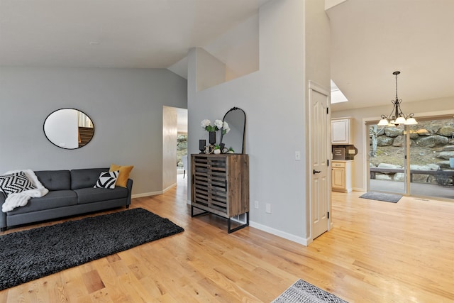 living area featuring an inviting chandelier, vaulted ceiling, baseboards, and light wood-type flooring