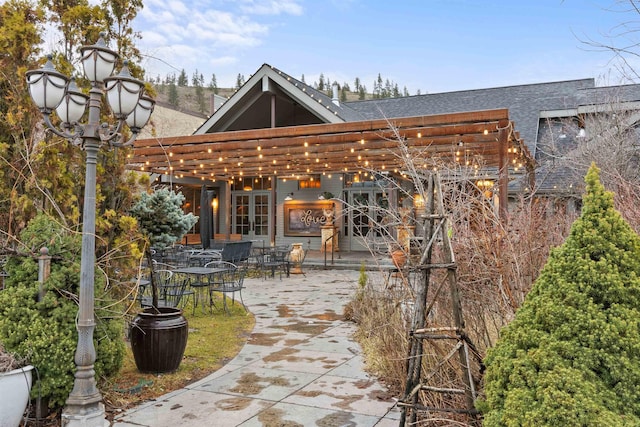 rear view of property with french doors, a shingled roof, outdoor dining area, and a patio