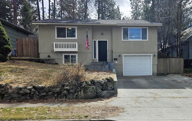 bi-level home with concrete driveway, a garage, and fence