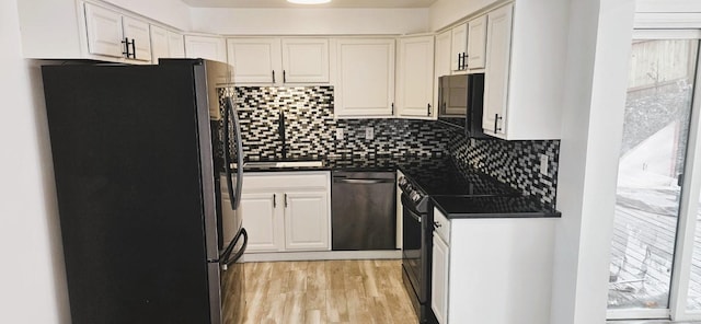 kitchen with dark countertops, backsplash, light wood-style flooring, white cabinets, and black appliances