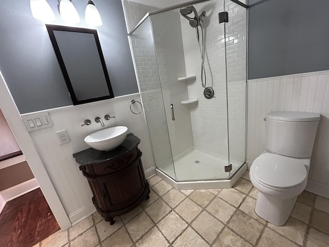 full bath with toilet, a stall shower, stone tile floors, wainscoting, and vanity