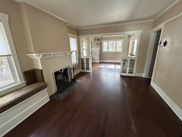 unfurnished living room featuring dark wood-type flooring, ornamental molding, an inviting chandelier, baseboards, and a brick fireplace