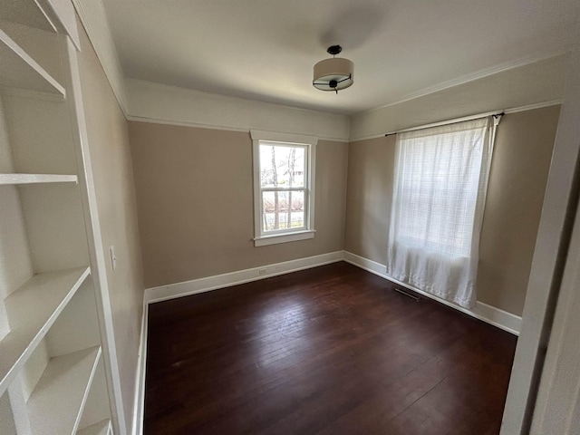 empty room with dark wood-style floors, visible vents, and baseboards