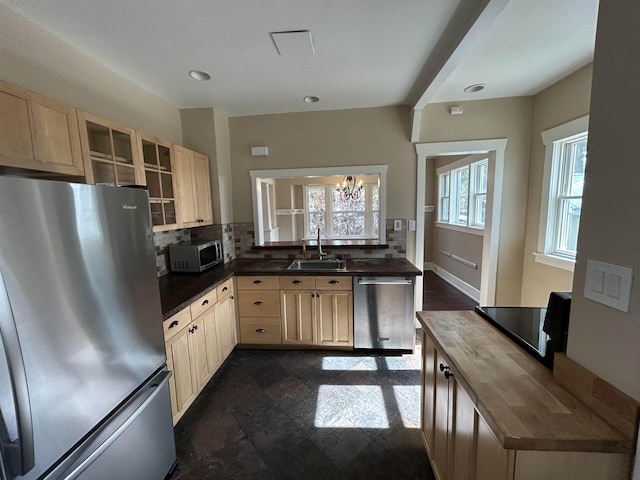 kitchen featuring light brown cabinetry, a sink, backsplash, stainless steel appliances, and glass insert cabinets