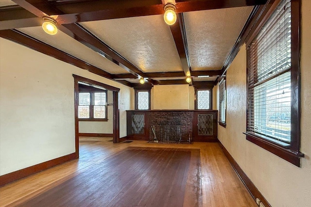 unfurnished living room featuring beamed ceiling, hardwood / wood-style flooring, coffered ceiling, baseboards, and ceiling fan