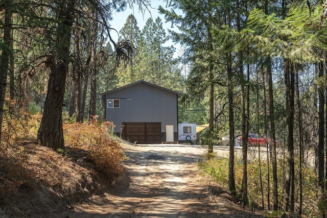 view of home's exterior with a wooded view, a garage, and dirt driveway