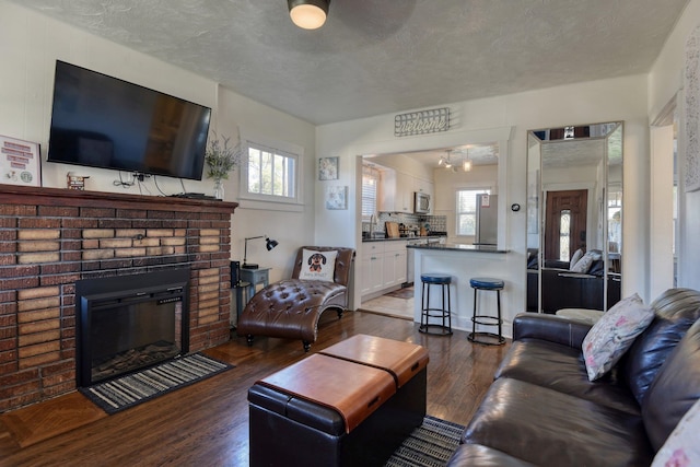 living area with a textured ceiling, a brick fireplace, and dark wood-style floors