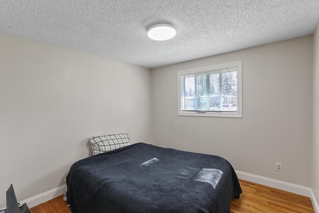 bedroom with baseboards, a textured ceiling, and wood finished floors