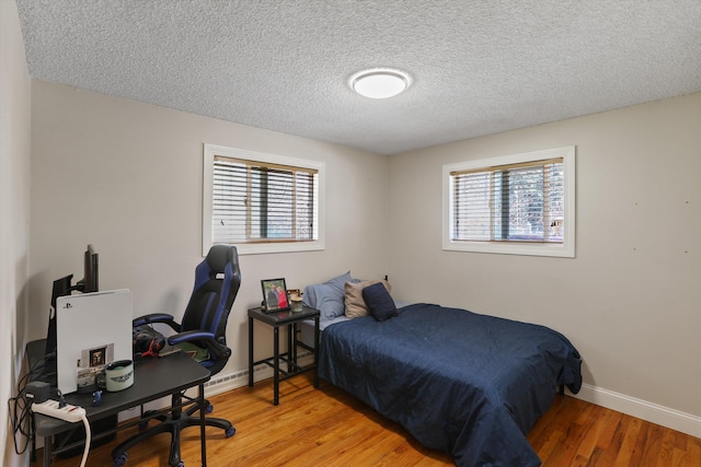 bedroom featuring light wood finished floors, multiple windows, a textured ceiling, and baseboards