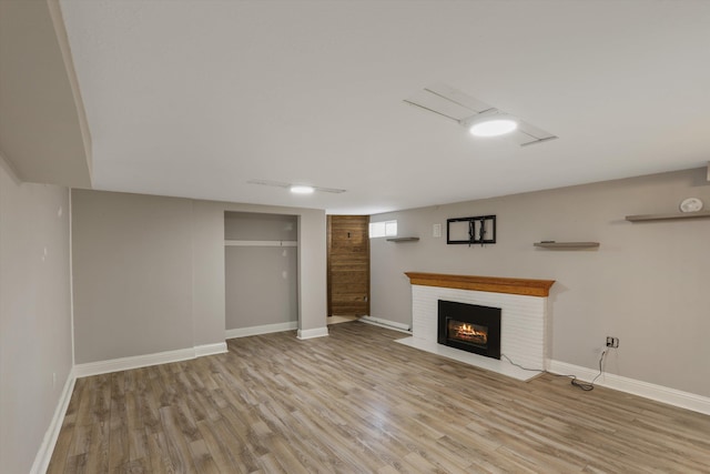 unfurnished living room featuring a brick fireplace, wood finished floors, and baseboards