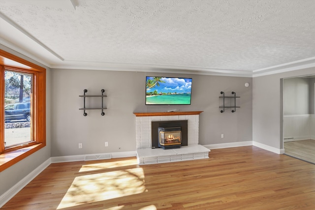 unfurnished living room with a brick fireplace, a textured ceiling, light wood-type flooring, and baseboards