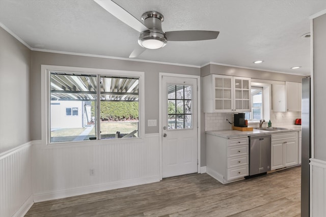 kitchen featuring ceiling fan, dishwasher, light countertops, wainscoting, and white cabinetry