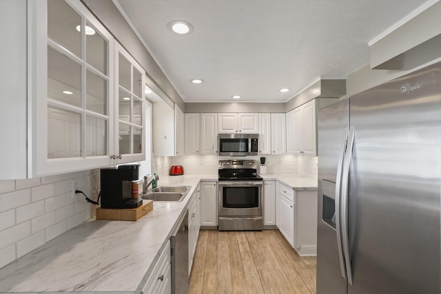 kitchen featuring light wood-style flooring, a sink, appliances with stainless steel finishes, white cabinets, and glass insert cabinets