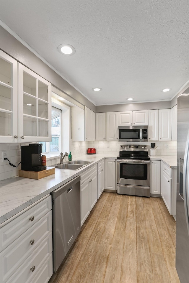 kitchen featuring light countertops, appliances with stainless steel finishes, light wood-style floors, white cabinets, and a sink