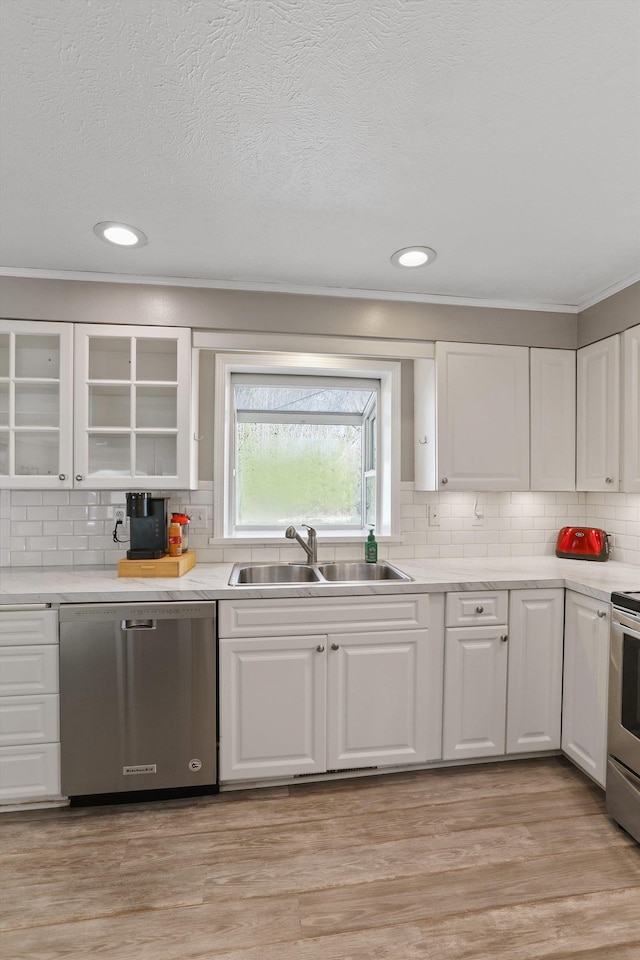 kitchen with light wood-style flooring, a sink, stainless steel appliances, white cabinets, and light countertops