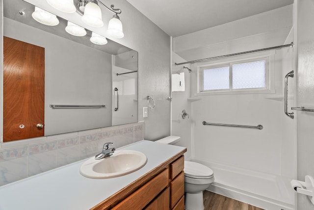 bathroom featuring toilet, tasteful backsplash, wood finished floors, a shower, and vanity