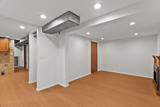 finished below grade area with recessed lighting, baseboards, light wood-style flooring, and a fireplace