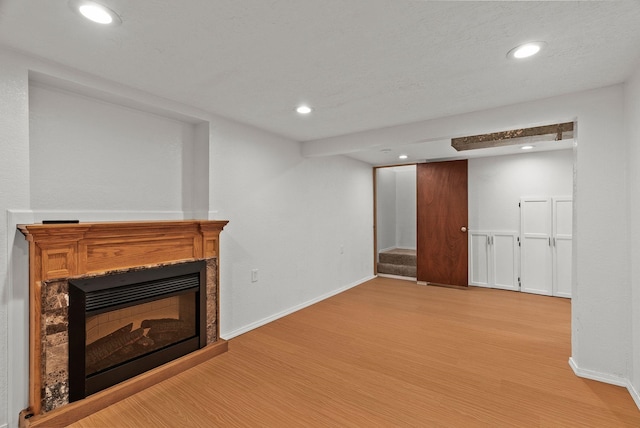 finished below grade area with recessed lighting, light wood-type flooring, a glass covered fireplace, and stairway