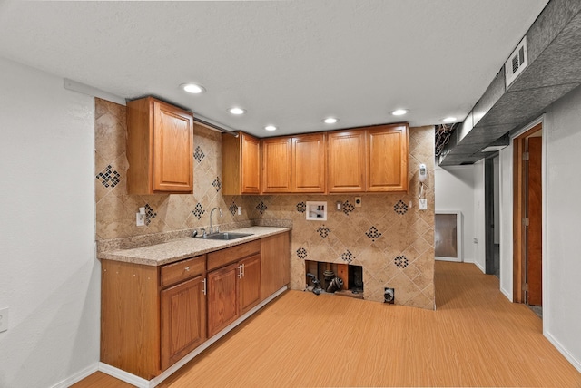 kitchen featuring light wood-style flooring, a sink, recessed lighting, brown cabinetry, and light countertops